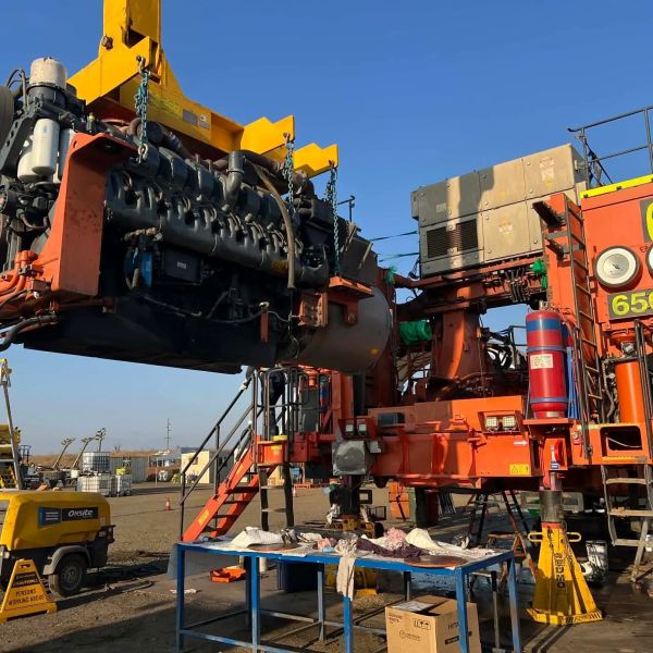 Heavy machinery lifting an engine at an industrial site.
