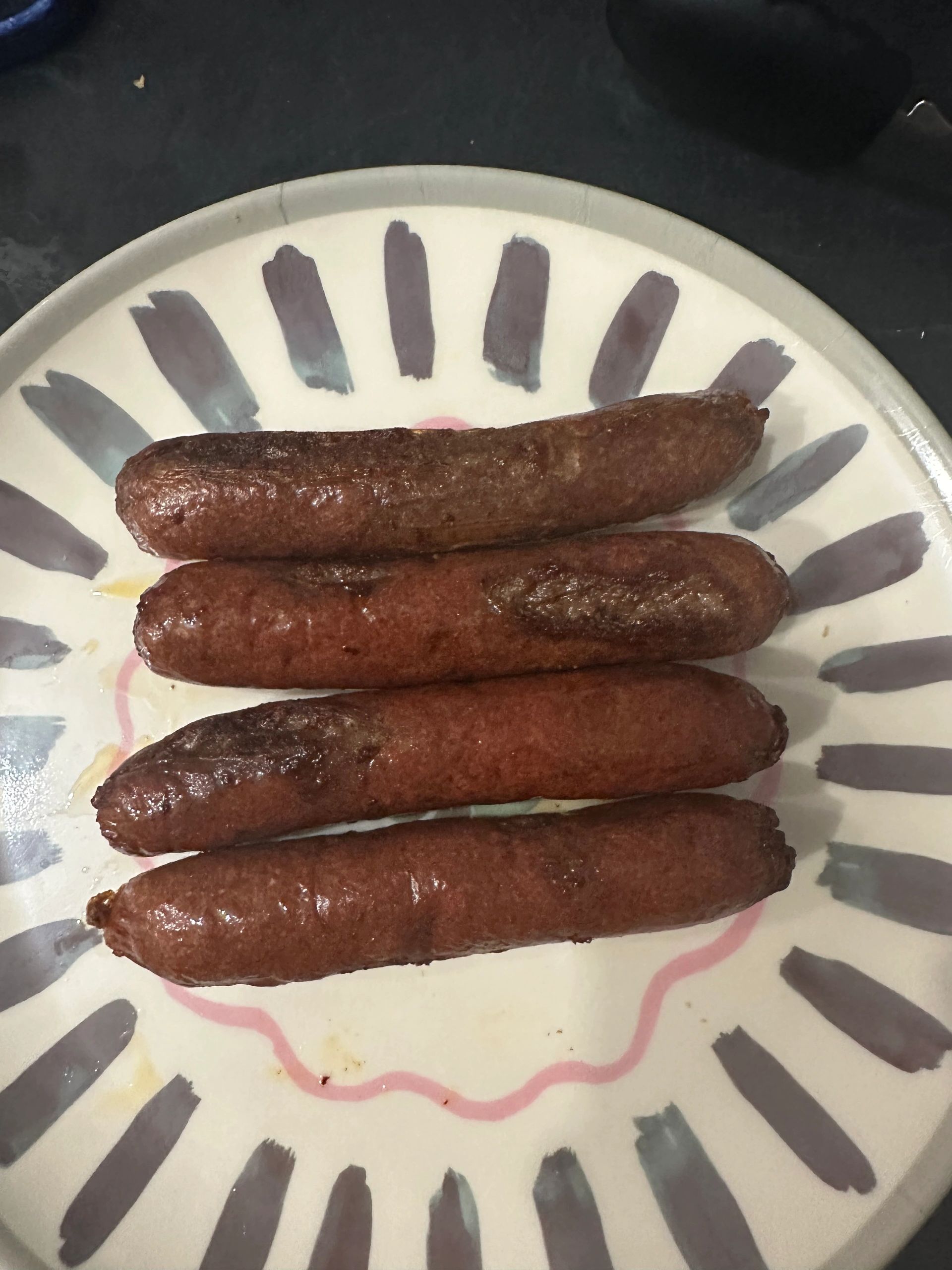Four cooked sausages on a decorative plate.