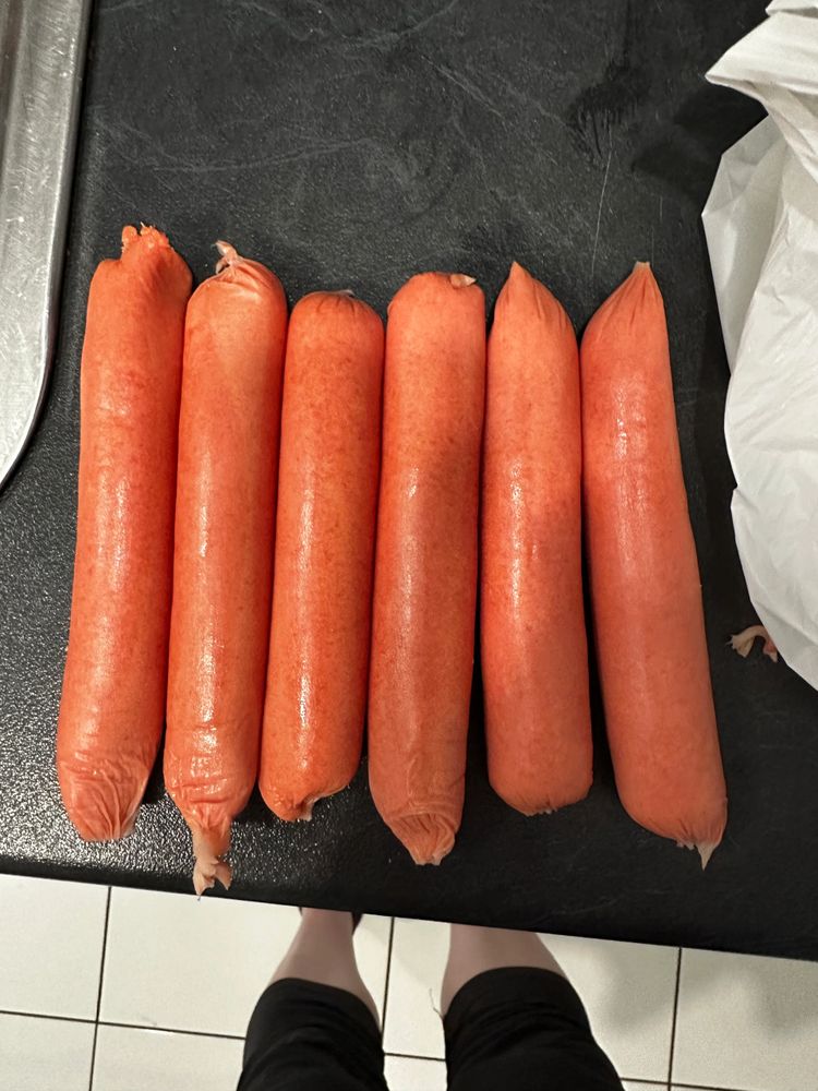 Six uncooked sausages lined up on a black countertop.