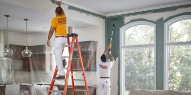 Two painters working on a living room ceiling and wall.