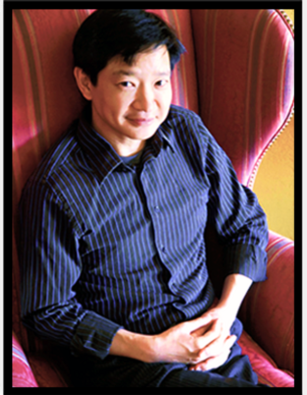 Ivan Chan, Psychotherapist, sitting in a chair with his hands in his lap and looking upwards.