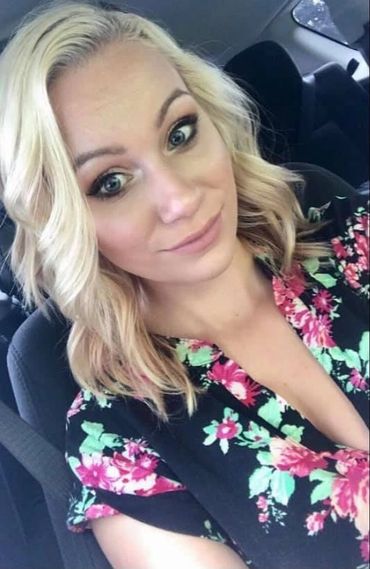 Smiling woman with blonde hair in a floral dress inside a car.