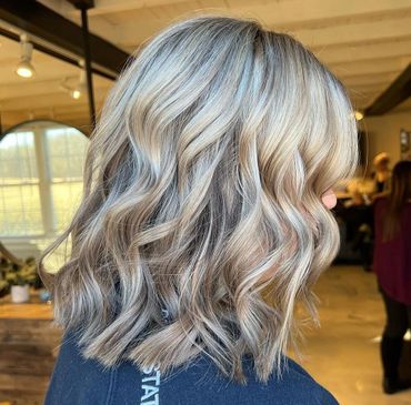 Wavy, shoulder-length silver blonde hair with dark roots in a cozy indoor setting.