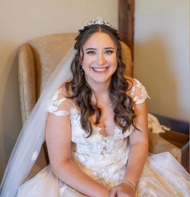 Smiling bride in a white wedding dress and tiara sitting on a chair.