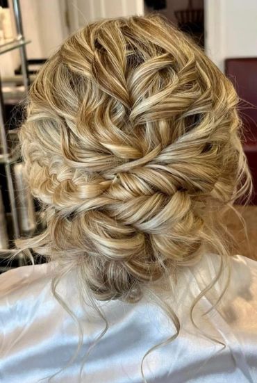 Intricate blonde braided updo hairstyle with loose curls.