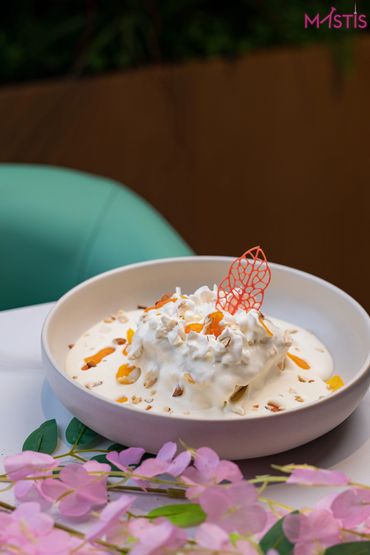 Creamy dessert with nuts and dried fruit in a bowl, garnished with an artistic red sugar decoration.