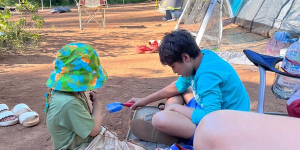 Two children playing outdoors near a tent, one wearing a colorful hat.