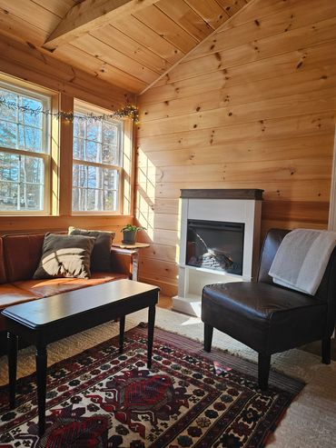 Cozy sunlit cabin living room with leather furniture and a fireplace.
