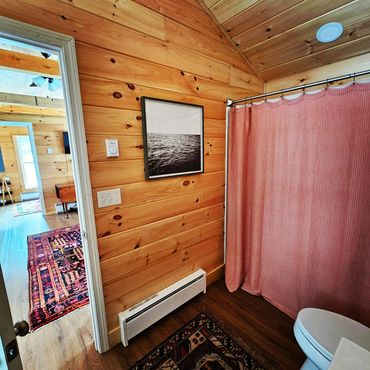 Cozy wooden bathroom with a pink shower curtain and patterned rugs.