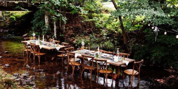 Dining tables set in a shallow stream surrounded by trees.