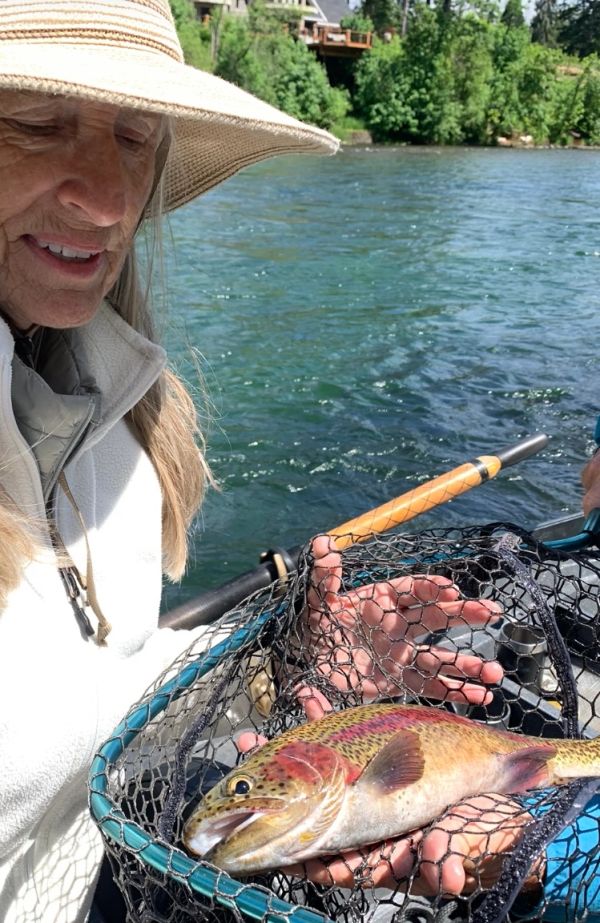 Woman holding a redside rainbow trout in a net on a McKenzie River drift boat.