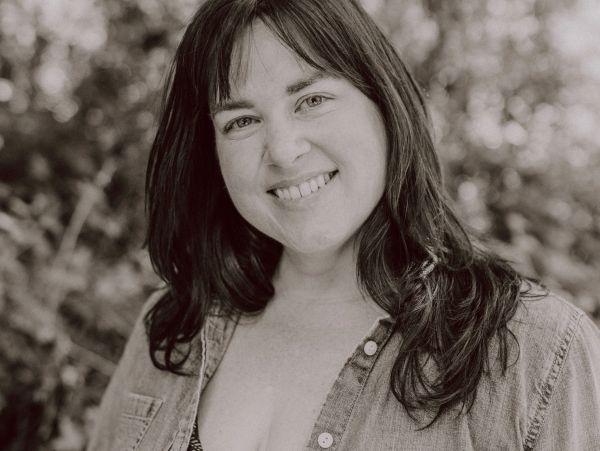 Smiling woman with long hair in a casual denim shirt outdoors.