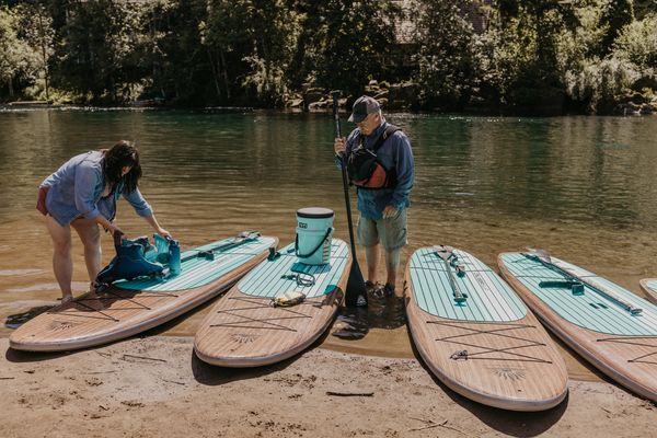 Two people preparing paddleboards by the water.