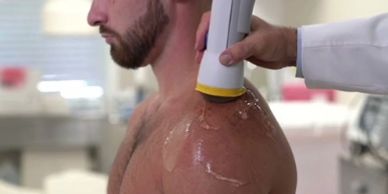 Man receiving ultrasound therapy on his shoulder in a clinical setting.