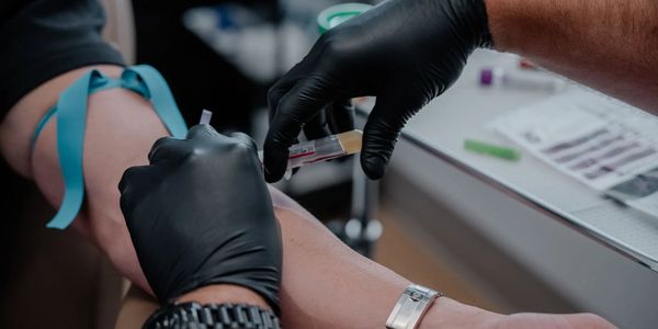 Healthcare worker draws blood from patient's arm wearing a blue tourniquet.