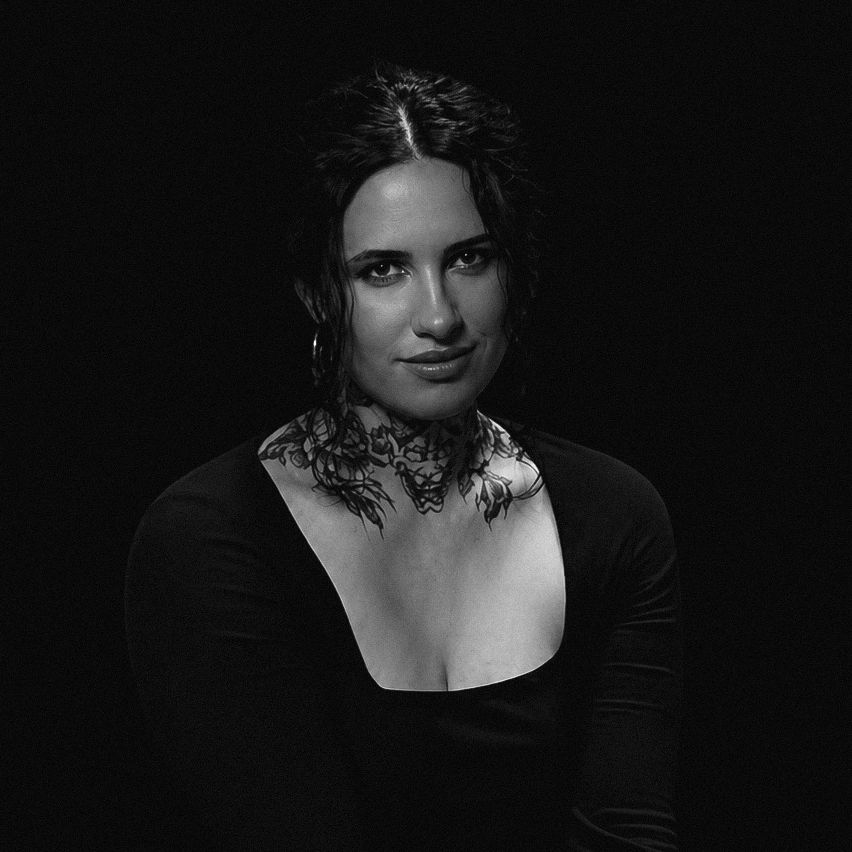Black and white portrait of a woman with a floral neck tattoo and confident expression.