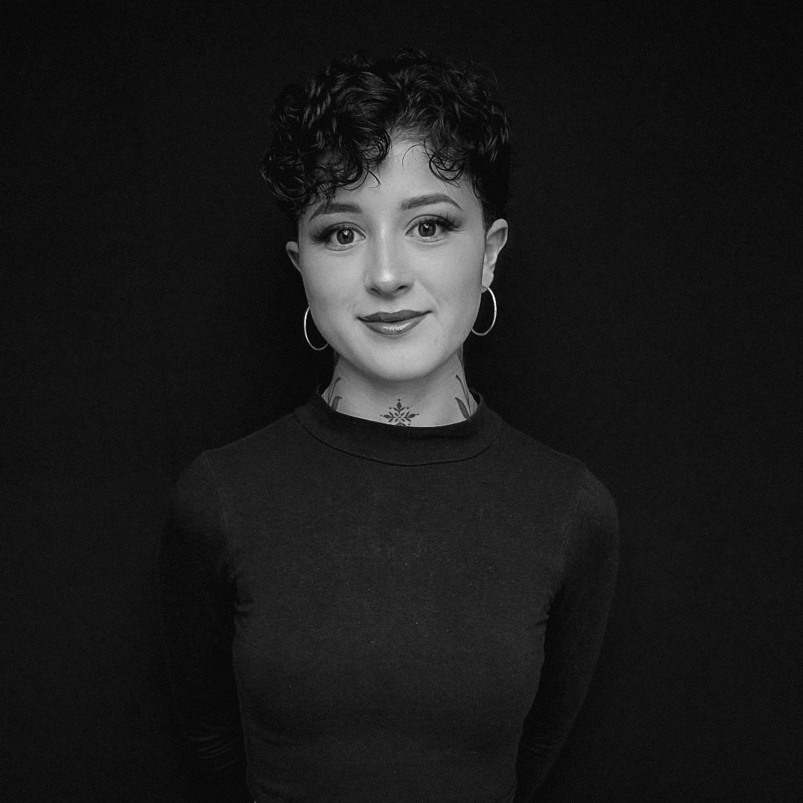 Young woman with short curly hair and hoop earrings against a black background.