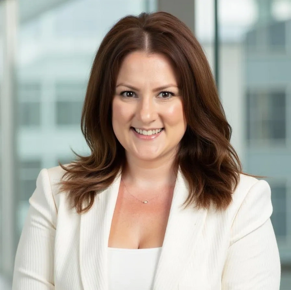 Professional woman with brown hair smiling in white blazer.