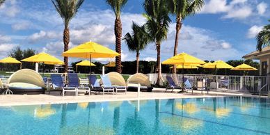 Poolside with yellow umbrellas and palm trees under blue sky.
