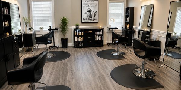 Modern and clean hair salon with black chairs and wooden flooring.