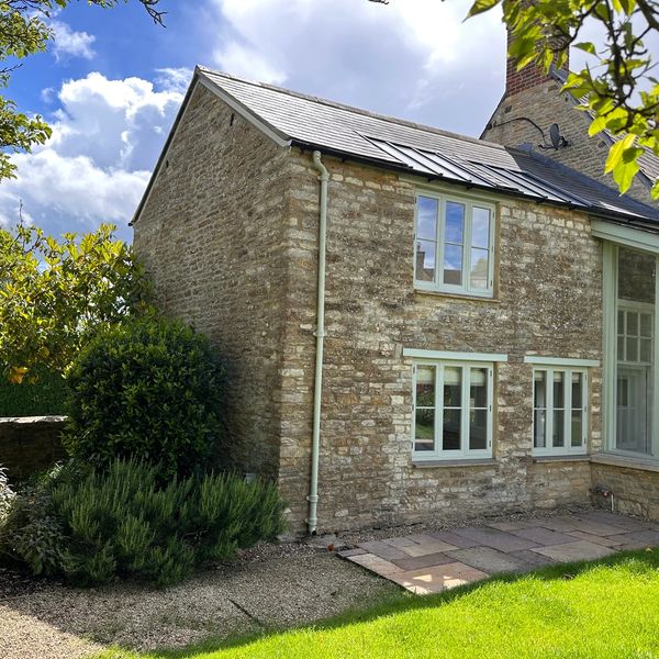 Stone house exterior with a garden and cloudy sky.