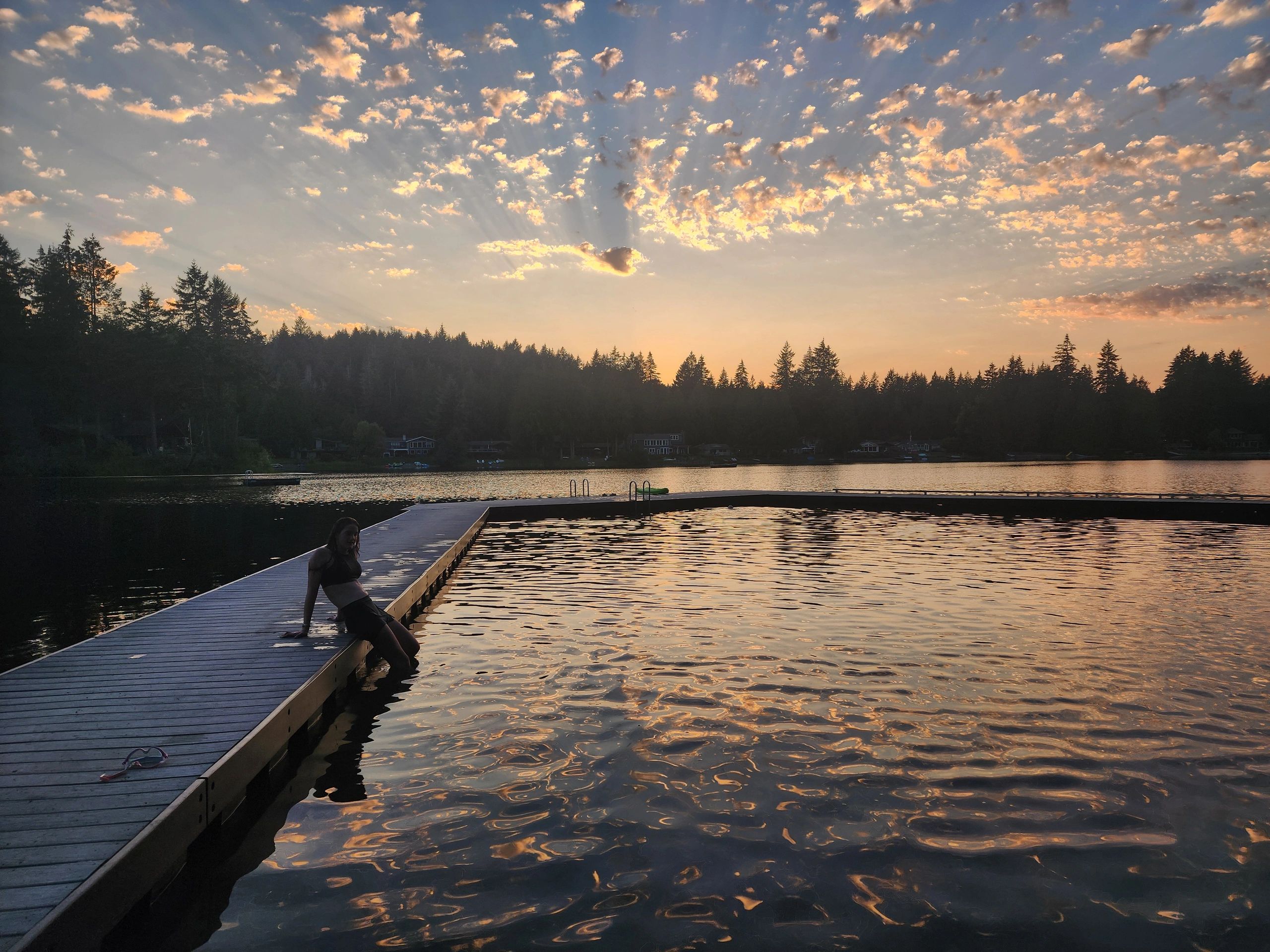 A person relaxing on a dock at sunset by a peaceful lake surrounded by trees.
