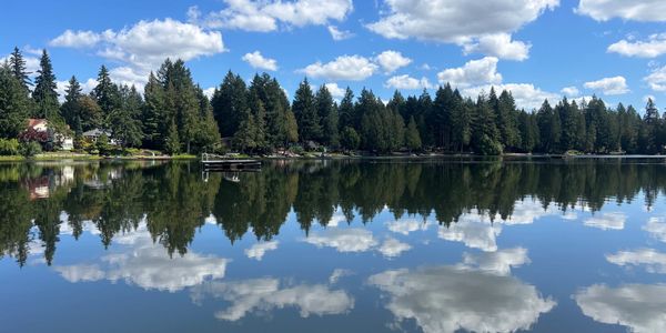 Calm lake with clear reflections of clouds and trees under a bright blue sky.