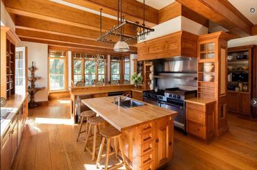 Warm wooden kitchen with island and large windows letting in natural light.