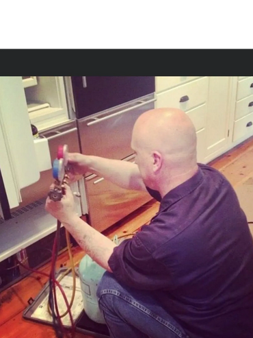 Technician servicing a refrigerator with HVAC gauges and refrigerant tank.