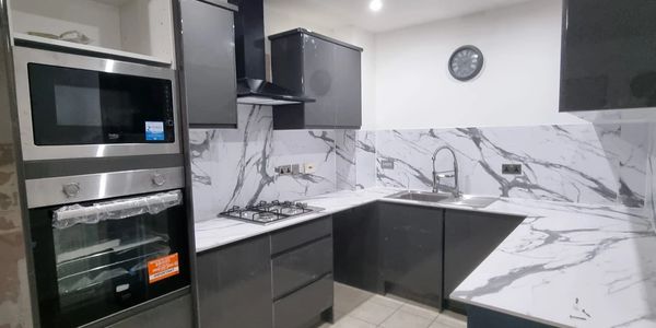 Modern kitchen with dark cabinets and marble countertops under bright ceiling lights.