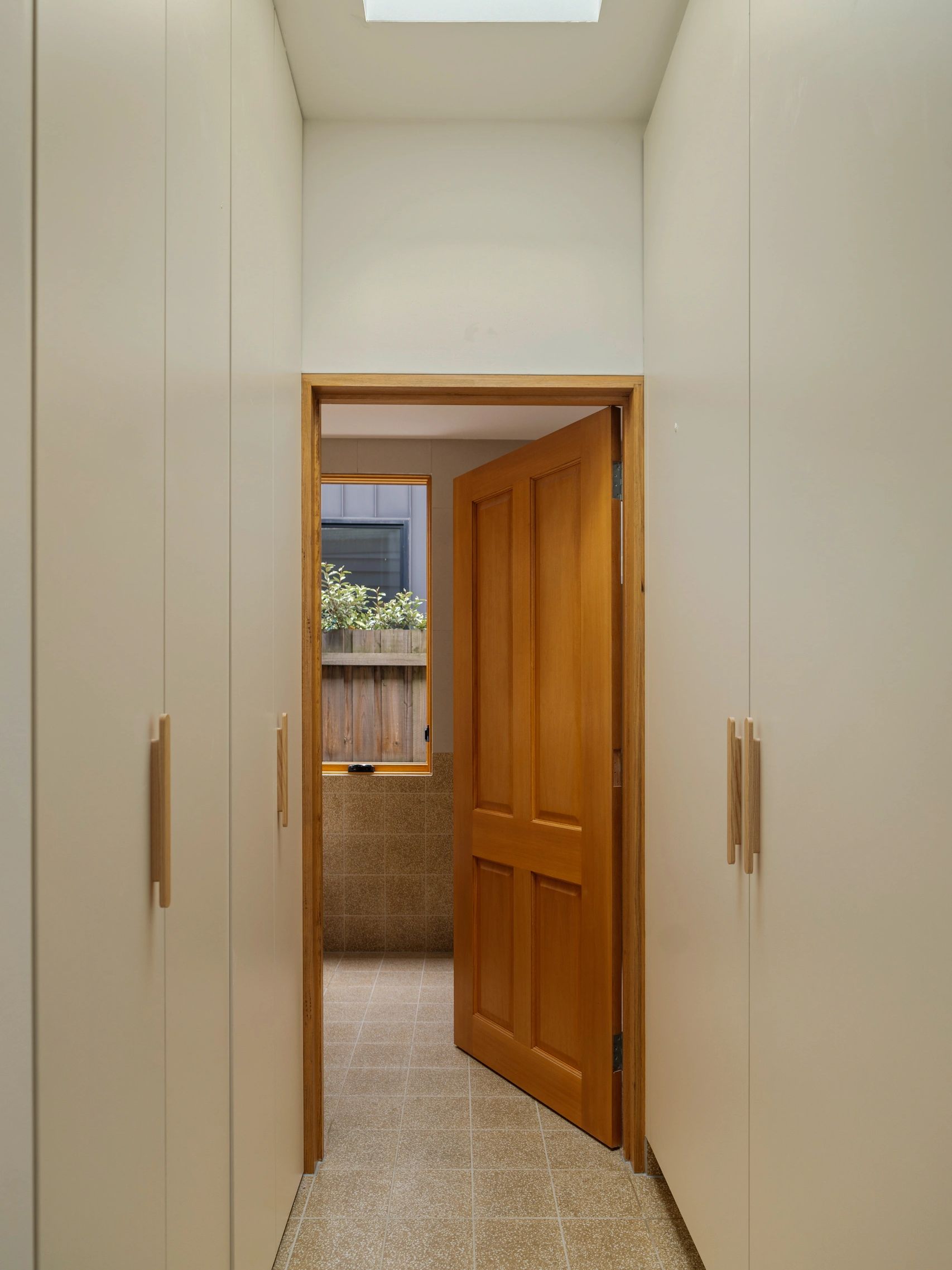 Solid timber door opening into bathroom, viewed past custom cabinetry, tiled floors and skylight