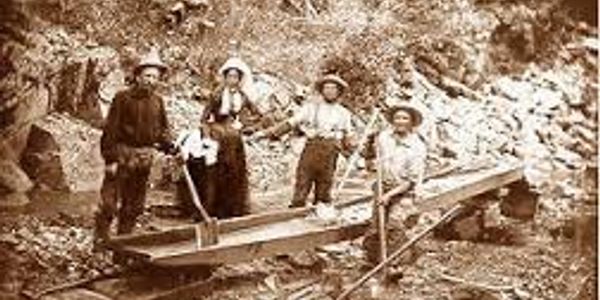 Four historical miners posing with mining equipment.