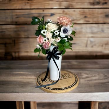 Elegant floral bouquet in a white vase with a black ribbon on a wooden surface.