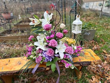 A vibrant flower arrangement with roses and lilies on a wooden bench outdoors.