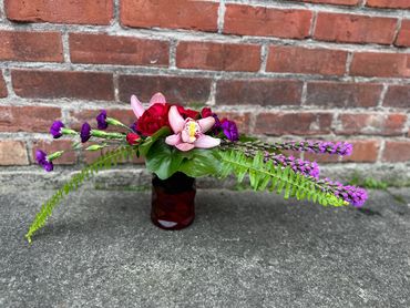 Elegant floral arrangement with red roses, pink orchid, purple flowers, and green leaves.