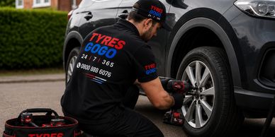 A mechanic changing a car tire outdoors with Tyres Gogo branding.