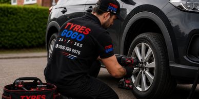 A mechanic changing a car tire outdoors with Tyres Gogo branding.