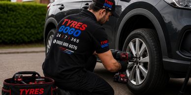A mechanic changing a car tire outdoors with Tyres Gogo branding.