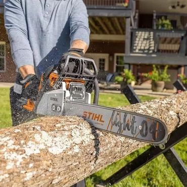 Person using a Stihl chainsaw to cut a large log outdoors.