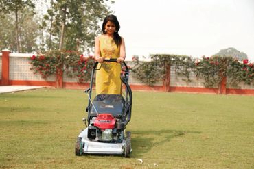A woman in a yellow dress mowing grass with a lawnmower.