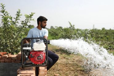 A man operates a water pump spraying water in a green field.