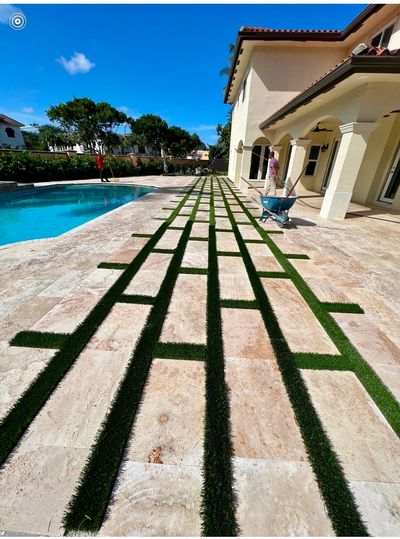 Artificial grass paver border called paver edging by a Miami pool on travertine deck