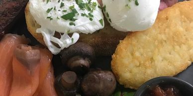 A hearty breakfast plate with poached eggs, ham, mushrooms, smoked salmon, hash brown, tomato, and chutney.