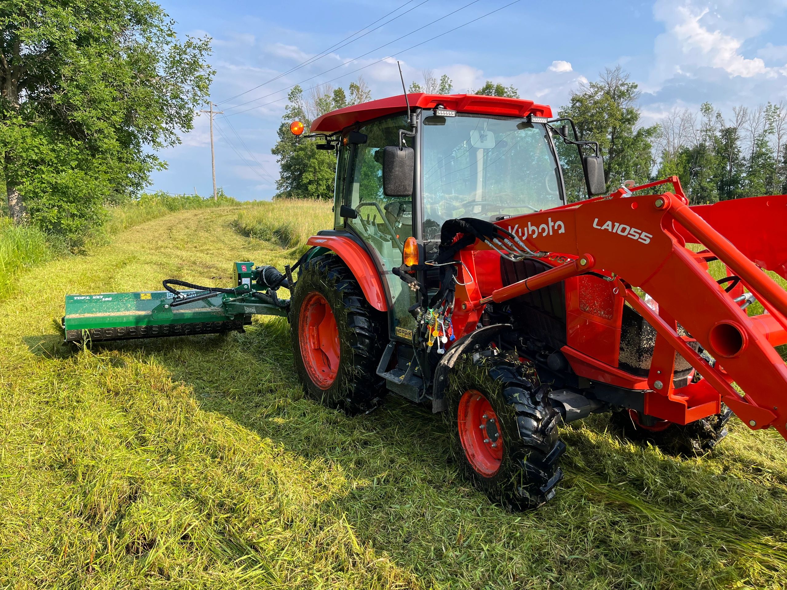 Red Kubota tractor working on a grassy field under a blue sky.