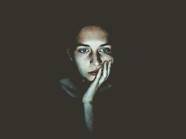 Person sitting in the dark with a pensive facial expression