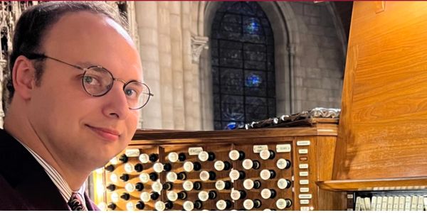 A man with glasses playing a large pipe organ in a grand church.