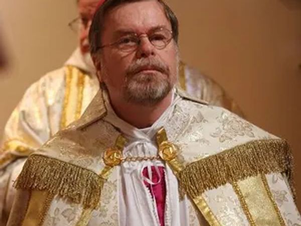 A man in ornate religious garments with glasses and a solemn expression.