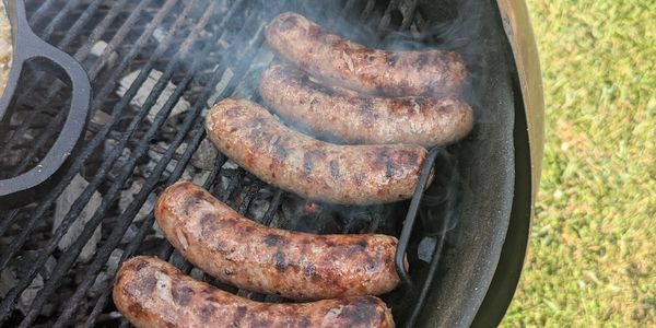 Beer brats searing over charcoal on a Weber kettle grill