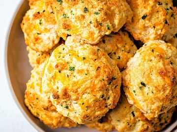Golden, crispy cheddar biscuits sprinkled with herbs in a bowl.