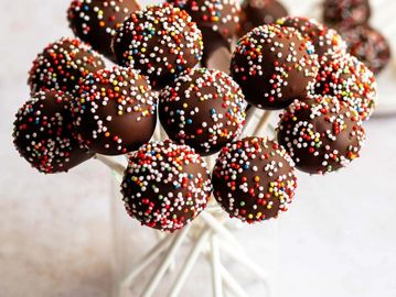 Chocolate cake pops with colorful sprinkles on white sticks.